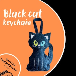 Puede incluir: Un llavero de gato negro con costuras blancas y un lazo para colgar. El gato tiene ojos amarillos y azules y detalles blancos. El texto "Black cat keychain" está encima del gato sobre un fondo naranja.