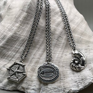 May include: Three silver necklaces with different pendants. The pendants are a starfish, a fish skeleton, and a nautilus shell.