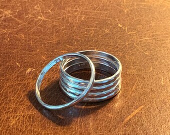 May include: Five silver rings stacked on top of each other. The rings are all hammered and have a textured surface.