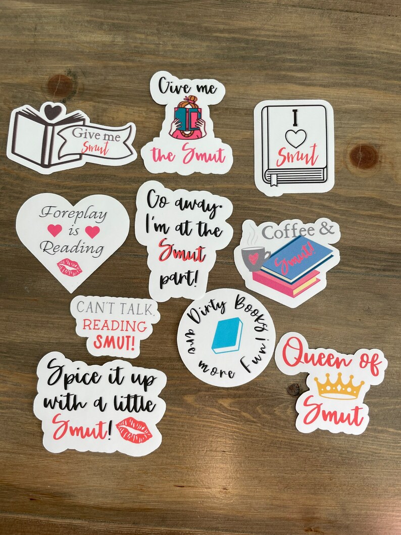 Op de afbeelding: Een set van tien stickers met verschillende boekenthema-ontwerpen en zinnen. De stickers zijn in verschillende kleuren, waaronder roze, rood, blauw en zwart. De zinnen op de stickers zijn: "Give me Smut", "Foreplay is Reading", "Give me the Smut", "I &hearts; Smut", "Go away. I'm at the Smut part!", "Coffee & Smut", "Can't talk, reading smut!", "Spice it up with a little Smut!", "Dirty Books are more fun" en "Queen of Smut".