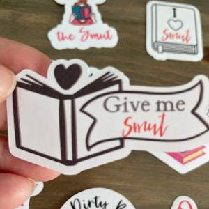 Op de afbeelding: Een set stickers met een boek met een hart op de omslag en de tekst "Give me Smut". Andere stickers zijn een vrouw die een boek leest met de tekst "Give me the Smut", een boek met een hart en de tekst "I &hearts; Smut", en een boek met de tekst "Dirty Books".