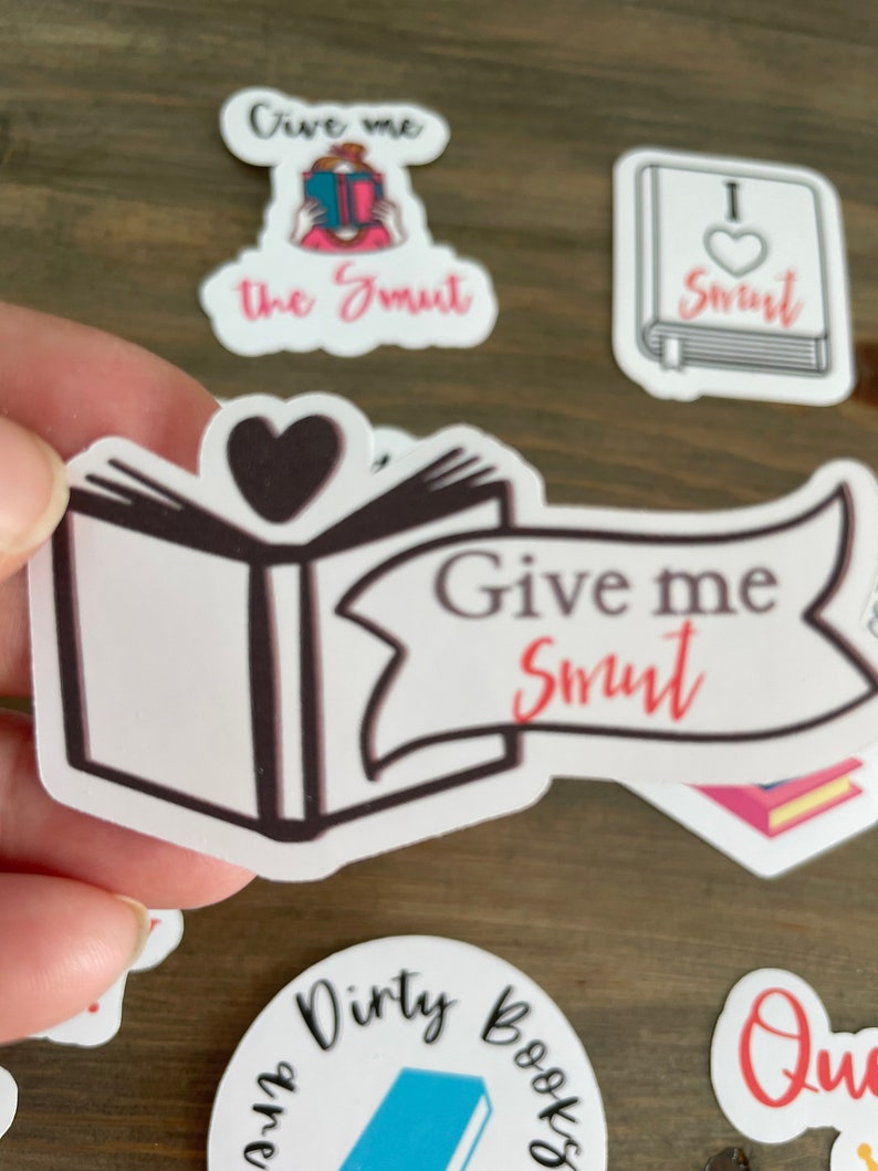 Op de afbeelding: Een set stickers met een boek met een hart op de omslag en de tekst "Give me Smut". Andere stickers zijn een vrouw die een boek leest met de tekst "Give me the Smut", een boek met een hart en de tekst "I &hearts; Smut", en een boek met de tekst "Dirty Books".