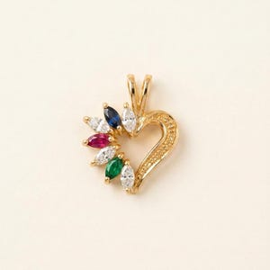 Puede incluir: Un colgante de oro en forma de corazón con una serie de piedras preciosas de talla marquesa en el lado izquierdo, incluyendo piedras transparentes, azules, rojas y verdes. El lado derecho tiene textura de pequeñas cuentas de oro y una reasa.