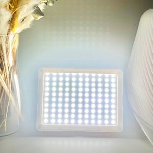 Peut inclure: Un Litho Light Box rectangulaire avec une grille de lumières LED blanches et brillantes. Le boîtier lumineux est encadré dans un cadre de couleur claire. Le texte "Litho Light Box" est affiché dans une bannière dorée en haut de l'image.