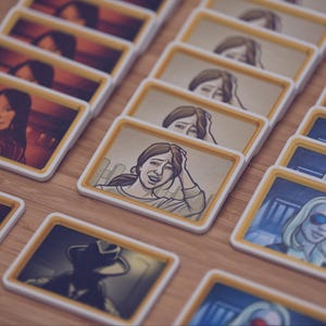 Pode incluir: Uma coleção de cartas de jogo retangulares com bordas brancas e molduras internas amarelas, cada uma apresentando um retrato de personagem ilustrado único. As cartas mostram vários indivíduos em diferentes cenários, incluindo alguns com tons de azul e vermelho.