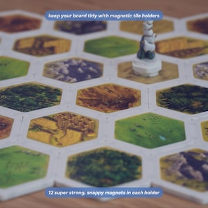 May include: A board game setup featuring hexagonal tiles held together by white magnetic tile holders. A small white game piece stands on one tile. Text on the image reads: keep your board tidy with magnetic tile holders and 12 super strong, snappy magnets in each holder.