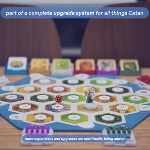 May include: A board game setup featuring a hexagonal blue frame containing various terrain tiles with numbered white circular tokens. A single red die and a grey figure are placed on the board. Text reads: part of a complete upgrade system for all things Catan, more expansions and upgrades are continually being added.