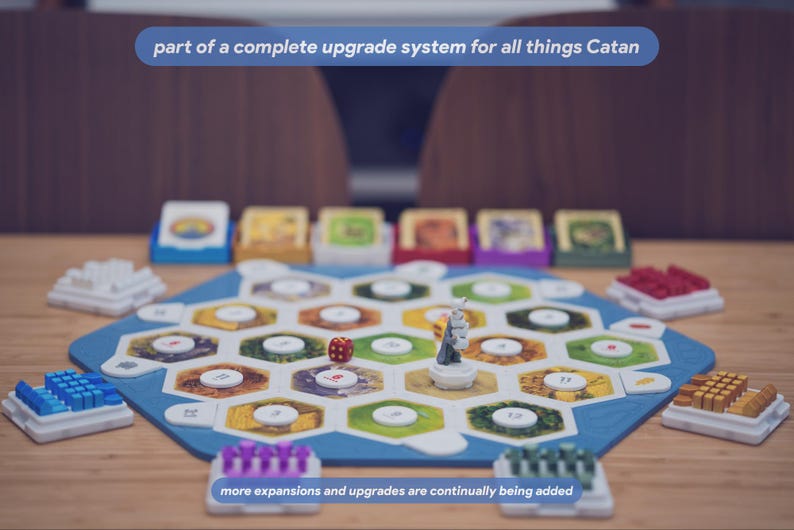 May include: A board game setup featuring a hexagonal blue frame containing various terrain tiles with numbered white circular tokens. A single red die and a grey figure are placed on the board. Text reads: part of a complete upgrade system for all things Catan, more expansions and upgrades are continually being added.