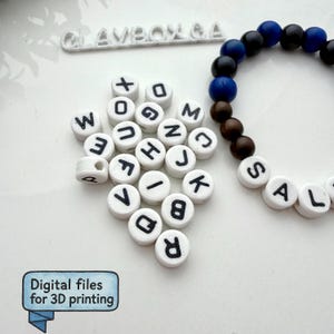 May include: A collection of white circular beads with black letters and numbers, alongside a bracelet with blue, black, and brown beads. The text "CLAVBOX GA" is visible. A blue box with the text "Digital files for 3D printing" is in the lower left corner.