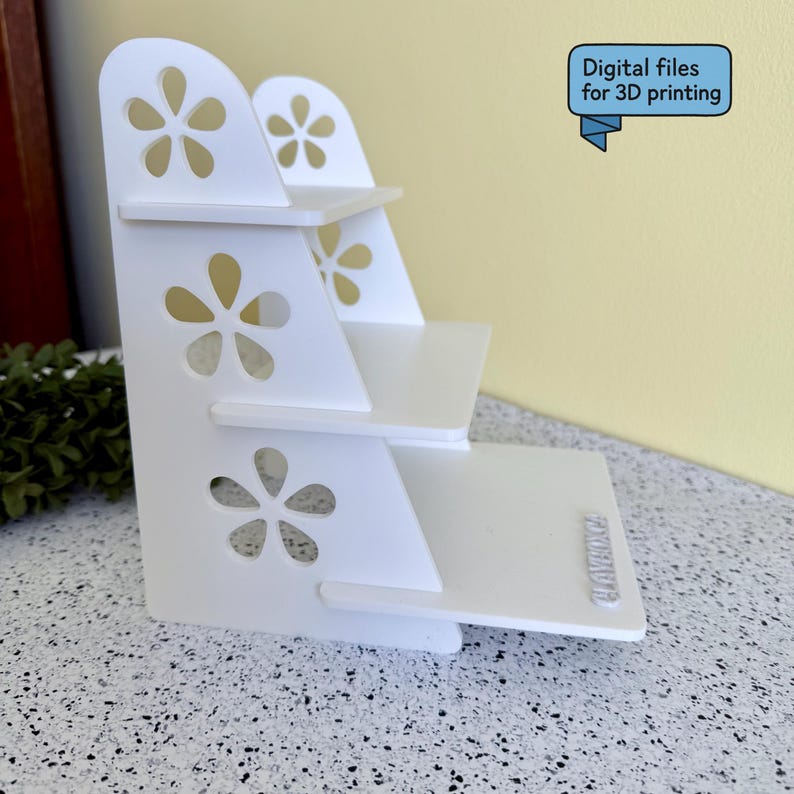 May include: A white, tiered display shelf with flower-shaped cutouts. The shelf has three levels and a rectangular base. Text on the image reads "Digital files for 3D printing."