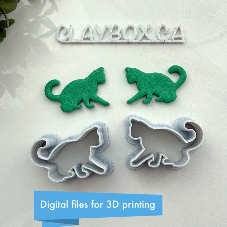 May include: Two 3D printed cat cookie cutters, one in white and one in green, with a white 3D printed sign that reads "CLAYBOX.CA".
