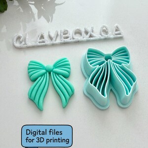 Op de afbeelding: Een turquoise boogvormig object en een turquoise boogvormige uitsteker liggen op een wit oppervlak. De uitsteker staat naast een 3D-geprinte boog. De tekst "CLAYBOXCA" staat boven de boog. De tekst "Digitale bestanden voor 3D-printen" staat eronder.