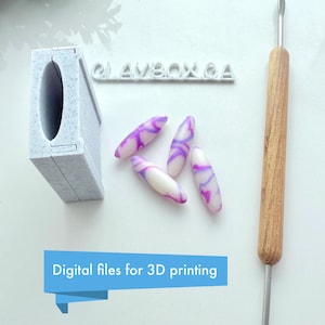 Op de afbeelding: Een 3D-geprinte mal voor het maken van polymer clay kralen. De mal is wit en heeft een rechthoekige vorm. Er liggen vijf paarse en witte swirl kralen naast de mal. Een houten gereedschap met een metalen punt is ook op de afbeelding te zien. De tekst "CLAYBOX & A" is zichtbaar op de mal. De tekst "Digitale bestanden voor 3D-printen" is zichtbaar onderaan de afbeelding.