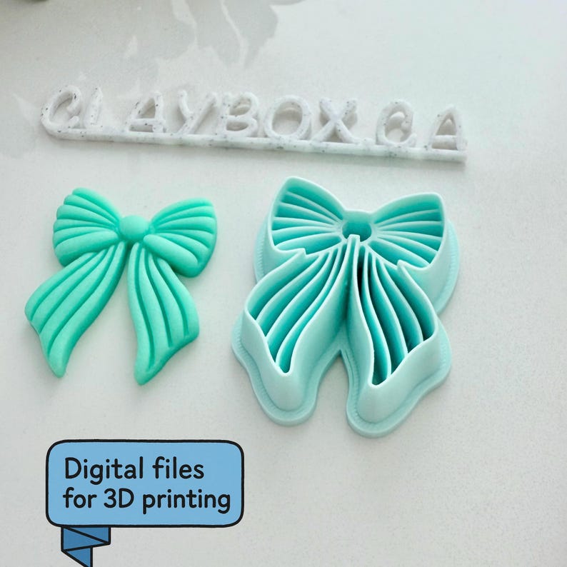 Op de afbeelding: Een turquoise object in de vorm van een strik en een strikvorm. De tekst "CLAYBOX CA" staat erboven. De afbeelding bevat ook een blauwe doos met de tekst "Digital files for 3D printing".