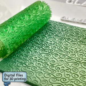 Puede incluir: Un rodillo cilíndrico de color verde translúcido con un patrón de remolinos en relieve y una placa verde plana a juego con el mismo diseño de volutas. Una pequeña etiqueta azul muestra el texto Digital files for 3D printing.