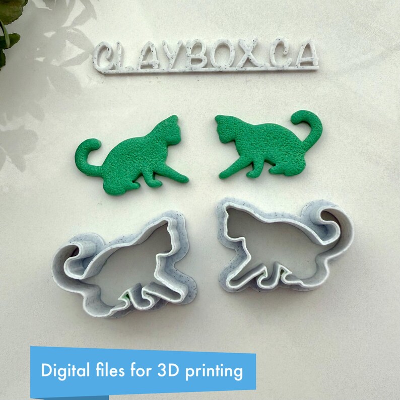 May include: Two 3D printed cat cookie cutters, one green and one white, with the text "CLAYBOX.CA" above them. Digital files for 3D printing.