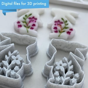 May include: Four 3D printed cookie cutters in the shape of bunnies with floral designs. Two cutters are white with pink flowers and two cutters are grey with white flowers.