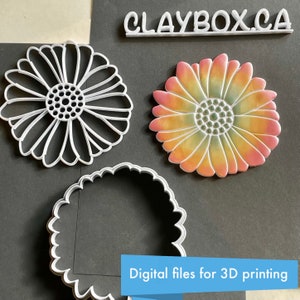May include: Three 3D printed cookie cutters, two are flower shaped and one is a circle. The flower cookie cutters are white and the circle cookie cutter is white with a scalloped edge. The background is black. The text "CLAYBOX.CA" and "Digital files for 3D printing" are visible in the image.