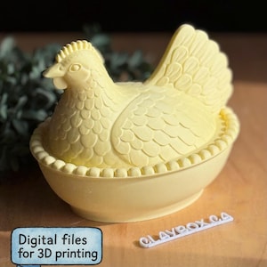 Könnte beinhalten: Ein hellgelber, huhnförmiger Behälter mit detailliertem Design, der in einer passenden nestartigen Basis sitzt. Der Behälter hat eine strukturierte Oberfläche und ist mit "Digital files for 3D printing" beschriftet.
