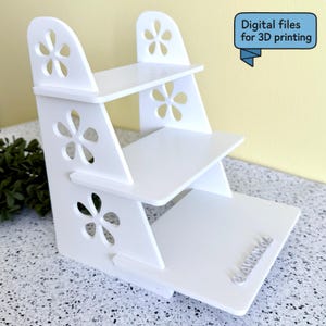 May include: A white, three-tiered display shelf with flower-shaped cutouts. The shelf has a stepped design and includes the text "Digital files for 3D printing" in a blue banner.