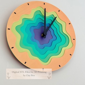 May include: A layered, colorful wall clock with a unique design. The clock features a series of concentric rings in shades of orange, green, blue, and purple. Black clock hands and hour markers complete the design. The text "Digital STL Files for 3D Printing by Clay Box" is at the bottom.