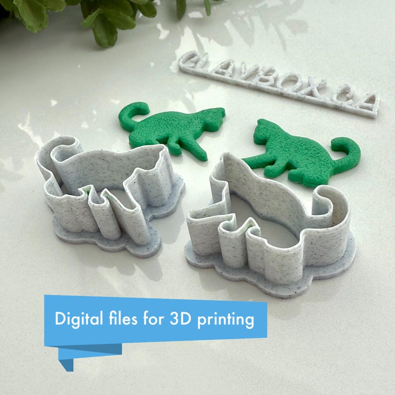 May include: Four 3D printed cookie cutters in the shape of cats. Two are white and two are green. The white cutters are designed for making cookies, while the green cutters are solid and appear to be for decoration. The text "CLAYBOX.CA" is visible in the background.