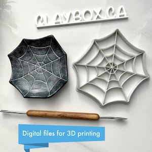 Op de afbeelding: Een zwart en grijs spinnenwebvormig schaaltje en een witte spinnenwebvormige mal. Een metalen en houten gereedschap bevindt zich onder het schaaltje en de mal. De tekst "CLAYBOX CA" staat erboven. De tekst "Digital files for 3D printing" staat eronder.