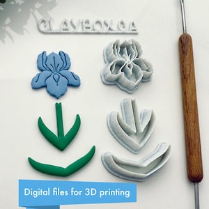 May include: A set of five 3D printed cookie cutters for making iris flowers. The cutters are in various shades of blue, green, and white. The text "CLAYBOX.CA" is visible at the top of the image. The image also includes a wooden tool for sculpting clay.