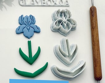May include: A set of five 3D printed cookie cutters for making iris flowers. The cutters are in various shades of blue, green, and white. The text "CLAYBOX.CA" is visible at the top of the image. The image also includes a wooden tool for sculpting clay.