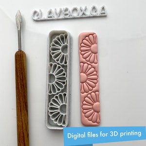 Puede incluir: Un sello de polímero impreso en 3D con un diseño de margarita. El sello es blanco y tiene una superficie texturizada. El sello se muestra junto a un sello de polímero rosa con el mismo diseño de margarita. El texto "CLAYBOX.CA" es visible en el fondo.