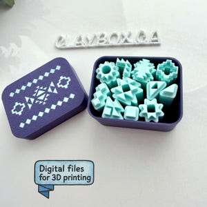 May include: A purple box with a geometric design and a separate container filled with light blue geometric shapes. The box lid is open, revealing the contents. The text "PLAYBOX.CA" is above the box. The text "Digital files for 3D printing" is below the box.