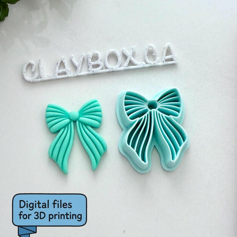Op de afbeelding: Twee turquoise strikvormige objecten, &eacute;&eacute;n massief en &eacute;&eacute;n een uitsteker, liggen op een wit oppervlak. Boven hen staat de tekst "CLAYBOX.CA" in het wit. Een blauw vak met de tekst "Digitale bestanden voor 3D-printen" staat linksonder.