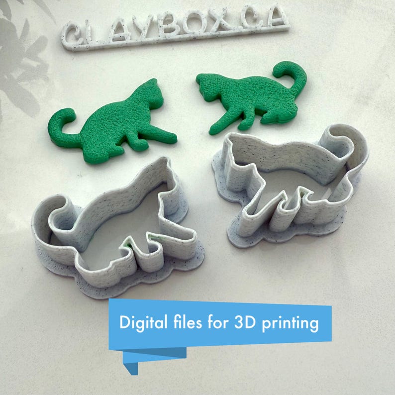 May include: Three 3D printed cat cookie cutters, two are white and one is green. The cutters are on a white surface. The text "CLAYBOX CA" is visible in the top left corner of the image. The text "Digital files for 3D printing" is visible in the bottom center of the image.