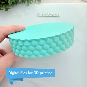 Könnte beinhalten: Ein türkisfarbener, ovaler Behälter mit einem strukturierten, blasenartigen Muster an den Seiten. Der Deckel hat einen gezackten Rand. Text auf einem blauen Banner: "Digitale Dateien für den 3D-Druck."