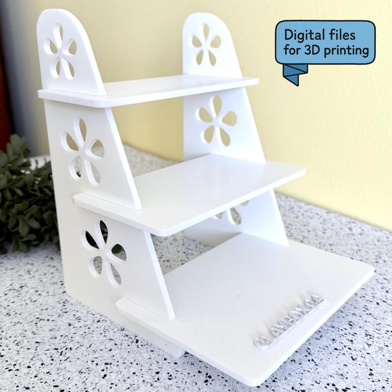 May include: A white, three-tiered display shelf with flower-shaped cutouts. The shelf has a stepped design and is made of a solid, opaque material. The text "Digital files for 3D printing" is in a blue banner. The shelf is suitable for displaying small items.