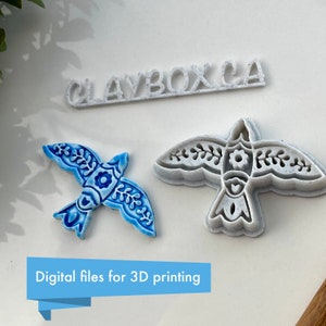 May include: Two 3D printed bird cookie cutters, one blue and white and one white. The blue and white bird has a floral design. The text "CLAYBOX.CA" is printed in white on a white background.