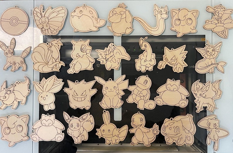 May include: A collection of wooden cutouts featuring various Pok&eacute;mon characters. The designs are laser-cut from light-colored wood, showcasing detailed outlines of each character. Includes a Pok&eacute;ball and several popular Pok&eacute;mon.