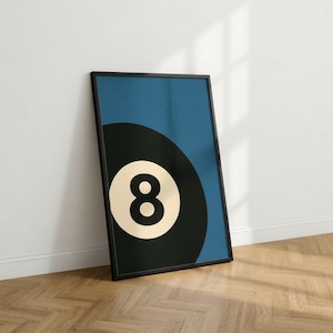 Könnte beinhalten: Gerahmter Kunstdruck mit einer schwarz-weißen Acht-Ball-Kugel vor blauem Hintergrund. Die Zahl 8 ist weiß auf dem Ball dargestellt. Das Kunstwerk befindet sich in einem schwarzen Rahmen und lehnt an einer weißen Wand. Wanddekoration.