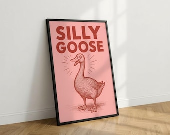 May include: A framed poster with the words "SILLY GOOSE" in red letters above a red illustration of a goose on a pink background. The goose is smiling with radiating lines. The frame is black.