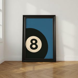 Puede incluir: Impresi&oacute;n art&iacute;stica enmarcada que presenta una bola ocho en blanco y negro sobre un fondo azul. La obra de arte est&aacute; enmarcada en negro y se apoya en una pared blanca sobre un suelo de madera. Dise&ntilde;o minimalista para una sala de juegos.