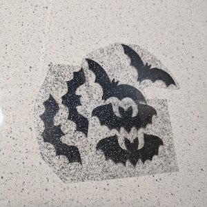 May include: A white surface with a black stencil of bats. The bats are arranged in a cluster, with some overlapping. The stencil is on a white background.