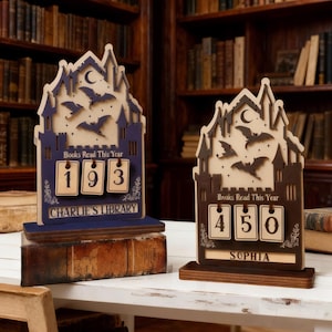 May include: Two wooden book counters in a castle design. One is navy blue with the text "Books Read This Year" and "193" displayed. The other is brown with "450" displayed. Both have a bat and moon design.