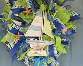May include: A nautical themed wreath with a wooden sailboat, blue and green striped ribbon, starfish, seashells, and white mesh.