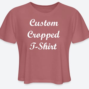 May include: A dusty rose cropped t-shirt with the words "Custom Cropped T-Shirt" in white script. The shirt has short sleeves and a relaxed fit, perfect for casual wear. The fabric appears soft and comfortable.
