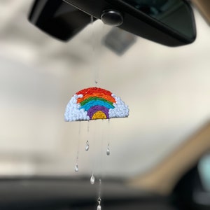 May include: A rainbow and cloud car charm with white beads hanging from the bottom, resembling raindrops.