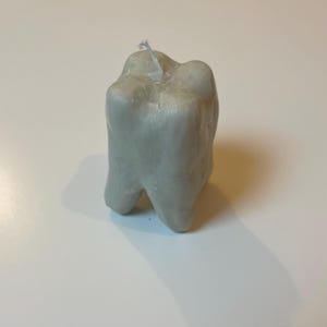 Peut inclure: Une bougie grise de forme irrégulière avec une mèche blanche.