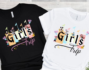 Könnte beinhalten: Zwei T-Shirts, eines schwarz und eines weiß, mit einem grafischen Design eines bunten Schlosses mit dem Text "Girls Trip" und Comicfiguren.