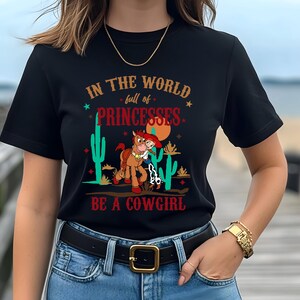 May include: Black t-shirt with a graphic of a cartoon cowgirl riding a horse with the text "In the world full of princesses be a cowgirl".