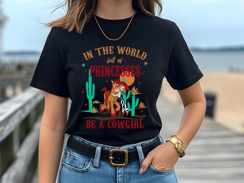 May include: Black t-shirt with a graphic of a cartoon cowgirl riding a horse with the text "In the world full of princesses be a cowgirl".
