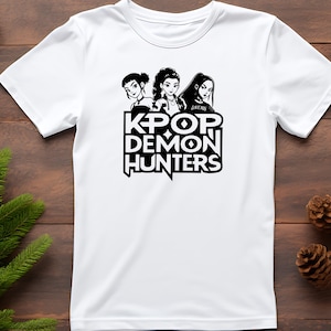 May include: White t-shirt featuring a black and white graphic of three stylized female figures above the text "KPOP DEMON HUNTERS". The design is centered on the front of the shirt.